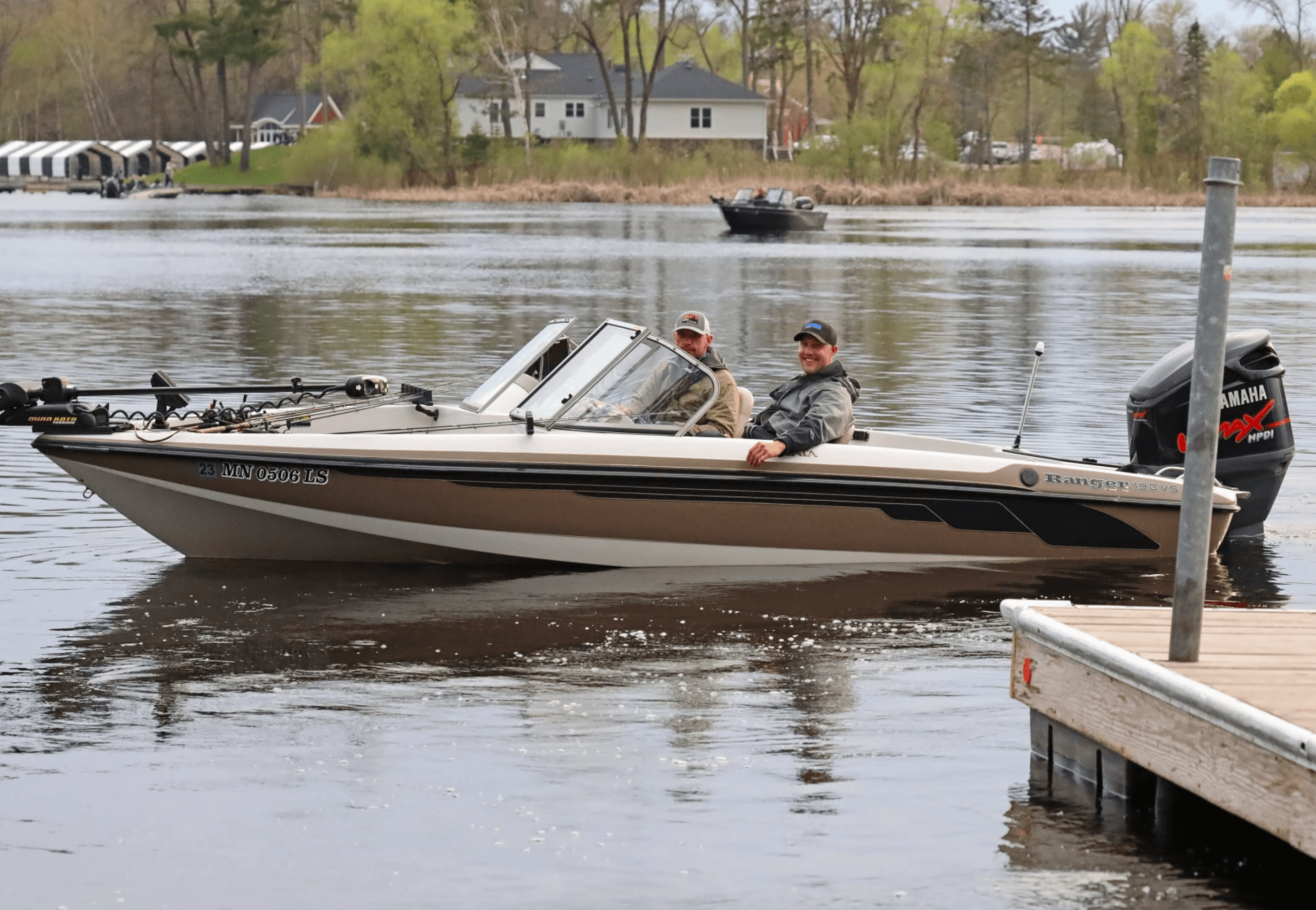 Two men in a Ranger motorboat on a lake, smiling near a wooden dock.