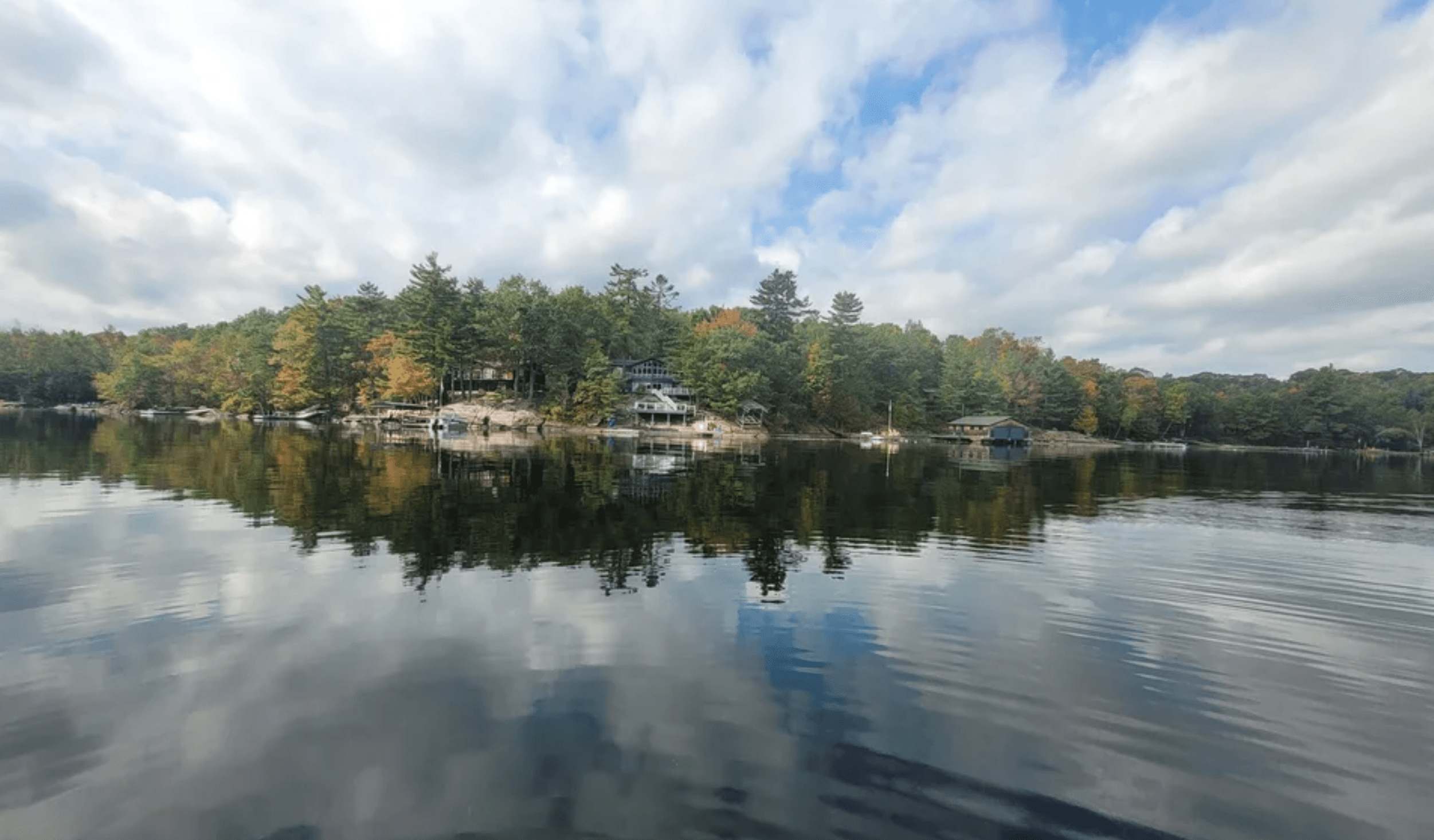 Cottages along a wooded shoreline reflecting in the calm water of a scenic lake.