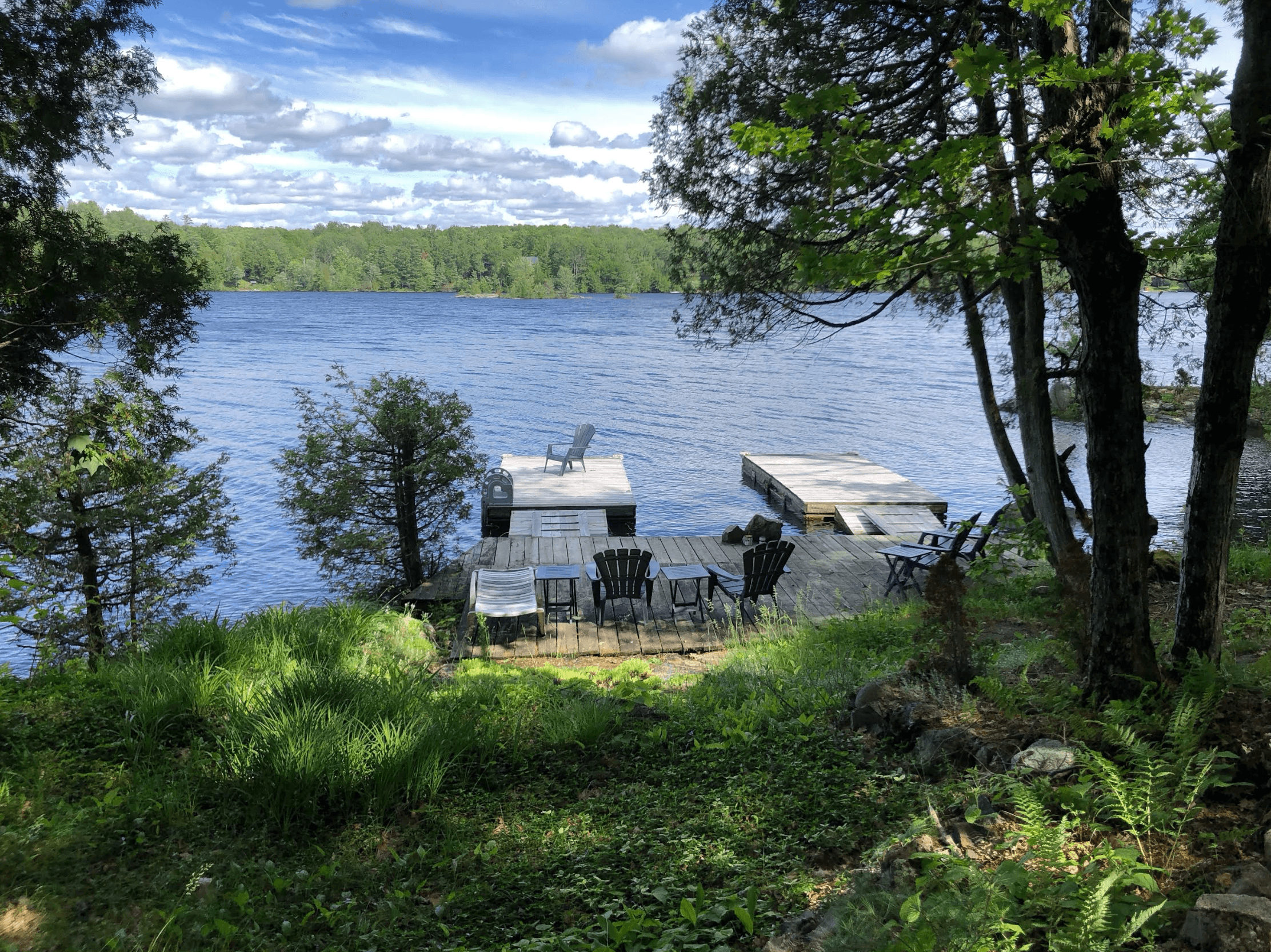 Adirondack chairs on a wooden dock overlooking a calm blue lake and green forest.